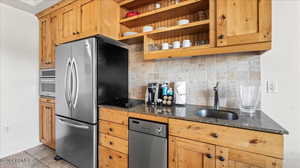 Kitchen featuring stainless steel appliances, sink, decorative backsplash, and dark stone countertops