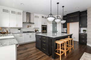 Kitchen featuring pendant lighting, white cabinetry, a center island, wall chimney exhaust hood, and stainless steel double oven.*Photos are of our Stella model home.  Actual colors and finishes will vary.  See agent for additional information.