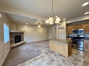 Kitchen with hanging light fixtures, a kitchen island, light colored carpet, stainless steel appliances, and a fireplace