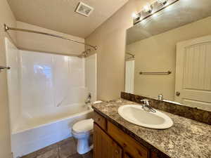 Full bathroom featuring toilet, a textured ceiling, vanity, shower / bath combination, and tile patterned flooring