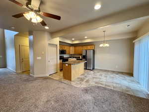 Kitchen with a kitchen island, dark stone countertops, hanging light fixtures, stainless steel appliances, and light carpet