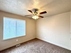 Empty room with ceiling fan, carpet floors, and a textured ceiling