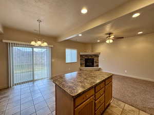 Kitchen with a stone fireplace, ceiling fan with notable chandelier, decorative light fixtures, light colored carpet, and a textured ceiling