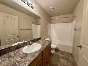 Full bathroom with toilet, vanity, a textured ceiling, and  shower combination