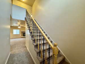 Staircase with a fireplace, ceiling fan, and carpet flooring