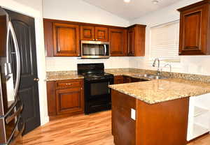 Kitchen with lofted ceiling, sink, appliances with stainless steel finishes, kitchen peninsula, and light hardwood / wood-style floors