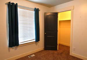 Unfurnished bedroom with a spacious closet, dark carpet, and a closet