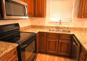 Kitchen featuring appliances with stainless steel finishes, sink, decorative backsplash, light stone countertops, and light hardwood / wood-style flooring
