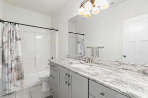 Full bathroom featuring toilet, an inviting chandelier, vanity, shower / bath combination with curtain, and tile patterned flooring