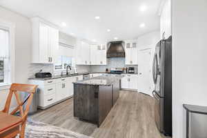 Kitchen featuring light stone counters, appliances with stainless steel finishes, a kitchen island, custom range hood, and white cabinets