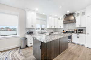 Kitchen with white cabinetry, custom exhaust hood, stainless steel appliances, and a center island