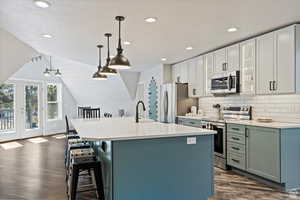 Kitchen featuring appliances with stainless steel finishes, hanging light fixtures, a center island with sink, dark hardwood / wood-style floors, and a kitchen bar