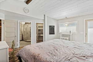 Bedroom with hardwood / wood-style flooring, ensuite bath, a walk in closet, and vaulted ceiling with beams