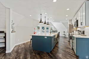 Kitchen featuring blue cabinetry, white cabinetry, stainless steel appliances, an island with sink, and decorative light fixtures