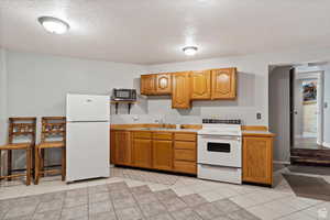 Kitchen with white appliances, sink, a textured ceiling, and light tile patterned floors