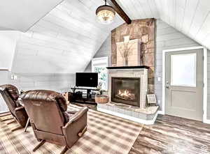 Living room with vaulted ceiling with beams, wood-type flooring, a large fireplace, and wood walls