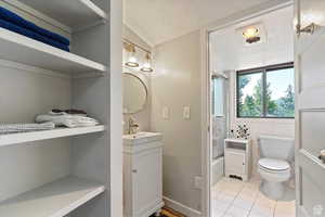 Full bathroom featuring shower / bath combination with glass door, vanity, toilet, tile patterned floors, and a textured ceiling