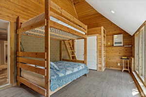 Unfurnished bedroom featuring vaulted ceiling, wood-type flooring, and wood walls