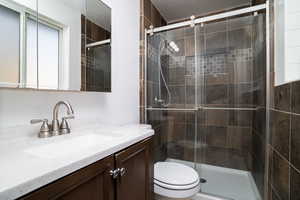 Bathroom featuring vanity, an enclosed shower, a textured ceiling, and toilet.