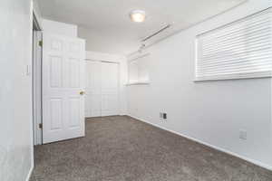 Unfurnished bedroom featuring a closet, rail lighting, dark carpet, and a textured ceiling