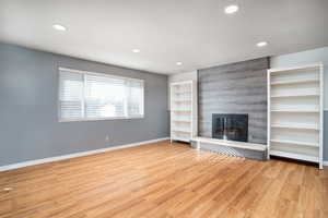 Unfurnished living room with a large fireplace, light hardwood / wood-style floors, and built in shelves