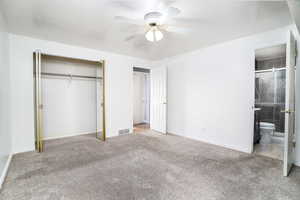 Unfurnished master bedroom featuring light colored carpet, a closet, ceiling fan, and ensuite bathroom.