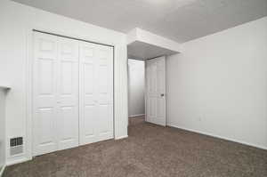 Unfurnished bedroom featuring dark carpet, a closet, and a textured ceiling