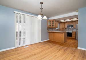 Kitchen featuring tasteful backsplash, decorative light fixtures, kitchen peninsula, stainless steel appliances, and light hardwood / wood-style floors