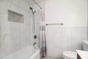 Full bathroom with shower / tub combo with curtain, vanity, toilet, and tile walls