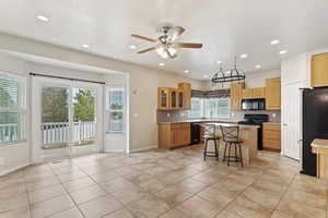 Kitchen featuring light tile patterned floors, a breakfast bar, backsplash, black appliances, and a kitchen island