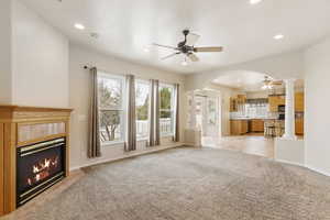 Unfurnished living room with ornate columns, light colored carpet, a fireplace, and ceiling fan