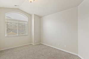 Carpeted spare room featuring vaulted ceiling