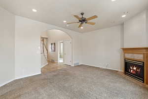 Unfurnished living room featuring light carpet, a tiled fireplace, and ceiling fan