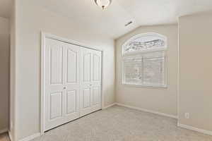 Unfurnished bedroom featuring lofted ceiling, light colored carpet, and a closet