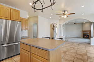 Kitchen with light tile patterned floors, stainless steel fridge, ceiling fan, a center island, and light brown cabinets