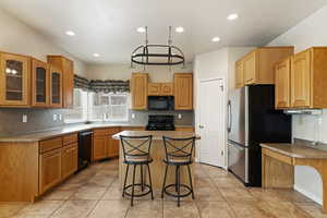 Kitchen with light tile patterned floors, a breakfast bar, black appliances, a kitchen island, and decorative backsplash