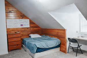 Carpeted bedroom featuring lofted ceiling, a textured ceiling, and wood walls