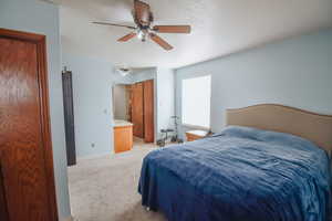 Bedroom featuring light carpet, a textured ceiling, ceiling fan, and ensuite bath