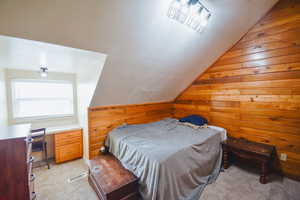 Bedroom featuring lofted ceiling, light carpet, and wood walls