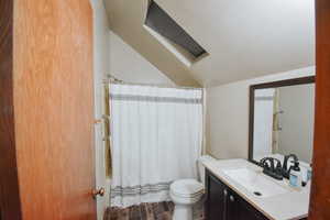 Full bathroom featuring shower / tub combo with curtain, lofted ceiling, vanity, toilet, and a textured ceiling