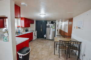 Kitchen with light tile patterned flooring, stainless steel refrigerator, sink, a textured ceiling, and electric stove