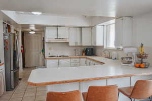 Kitchen with stainless steel fridge with ice dispenser, white cabinetry, sink, a kitchen breakfast bar, and kitchen peninsula