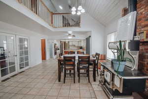 Dining room with ceiling fan with notable chandelier, high vaulted ceiling, french doors, and light tile patterned flooring