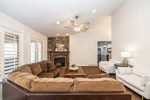 Living room with vaulted ceiling, a stone fireplace, carpet flooring, and ceiling fan