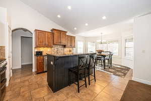 Kitchen with dark stone countertops, backsplash, a kitchen breakfast bar, a center island with sink, and decorative light fixtures