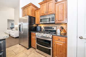 Kitchen featuring backsplash, light tile patterned flooring, dark stone counters, and appliances with stainless steel finishes