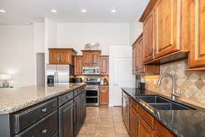 Kitchen featuring sink, light tile patterned floors, dark stone countertops, stainless steel appliances, and backsplash