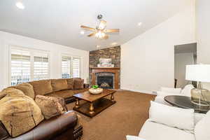 Living room with ceiling fan, lofted ceiling, carpet floors, and a fireplace