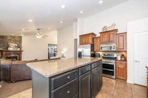 Kitchen featuring a center island, appliances with stainless steel finishes, a fireplace, light stone countertops, and decorative backsplash