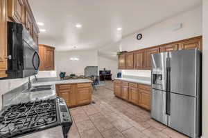 Kitchen with lofted ceiling, sink, hanging light fixtures, stainless steel appliances, and an inviting chandelier